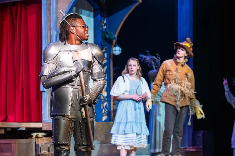 The Tin Man, Dorothy and the Scarecrow stand together on stage in a production of The Wizard of Oz.