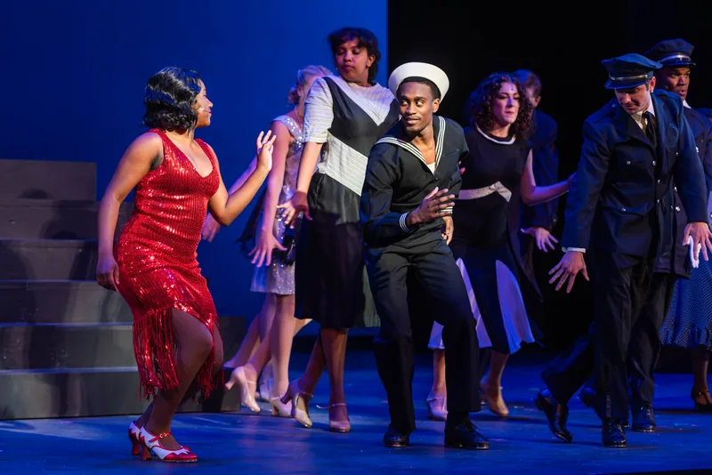 A woman in a red sequined dress dances beside a sailor and an officer in a lively ensemble scene.
