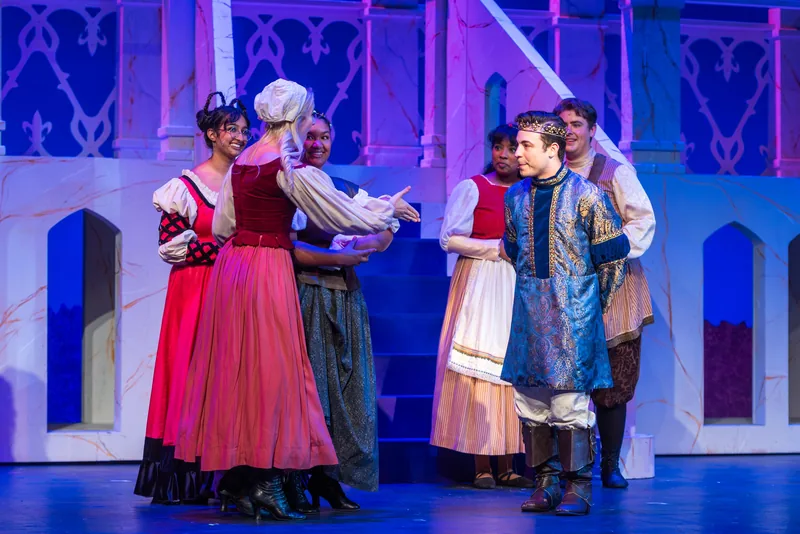 Actors in Renaissance-style costumes gather on a pale castle set lit in blue.
