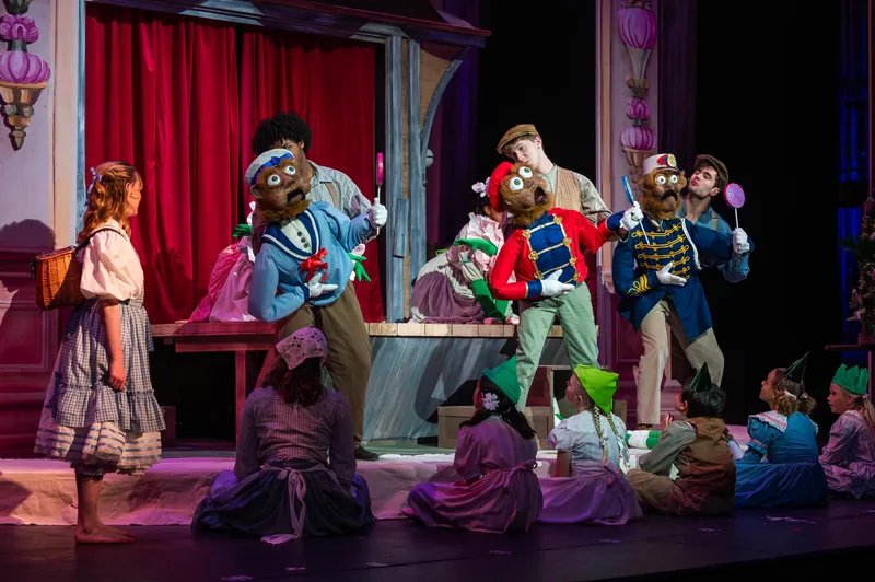 Life-size toy soldiers and gingerbread characters surround a girl on a storybook set.